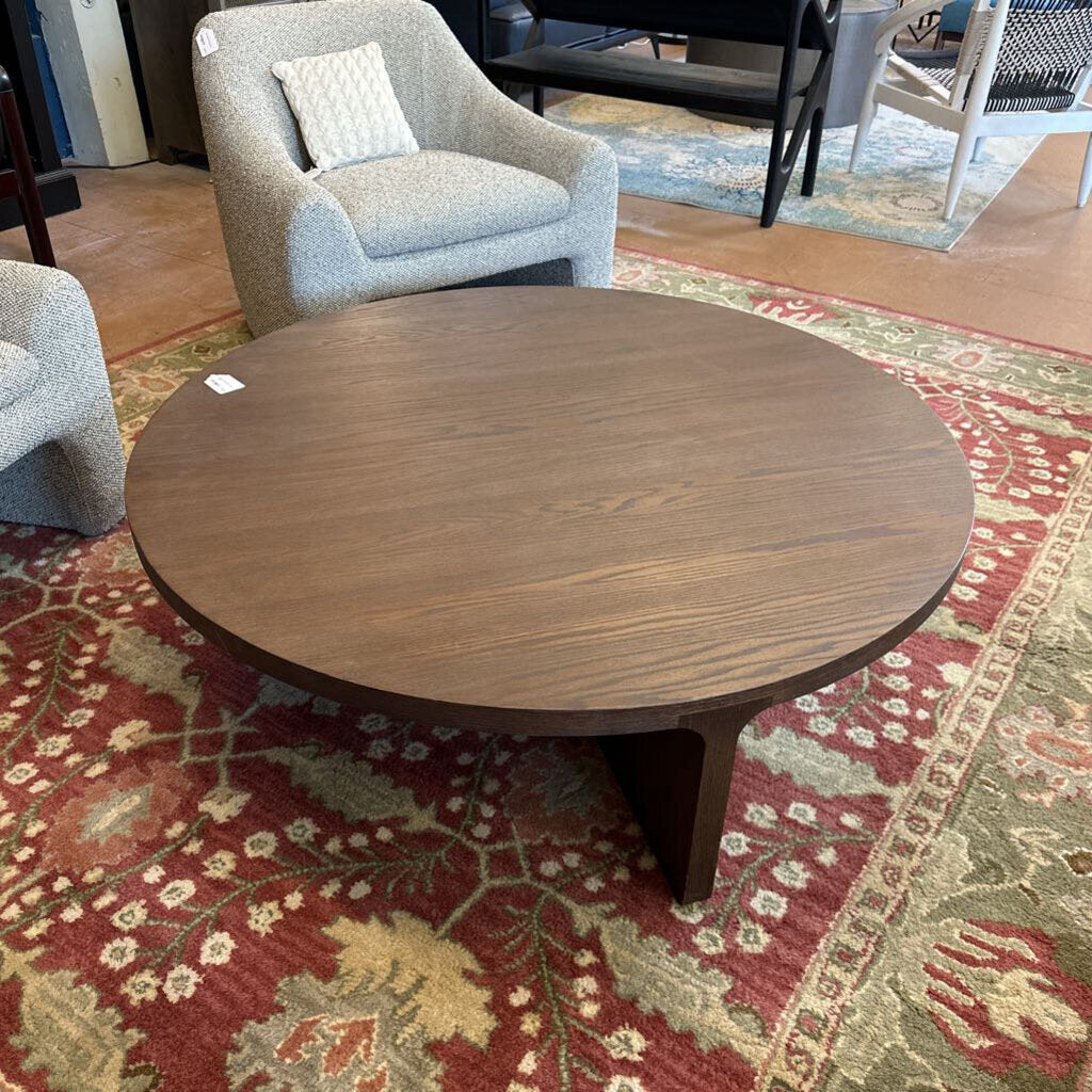 Round wooden coffee table on a patterned rug with chairs in the background