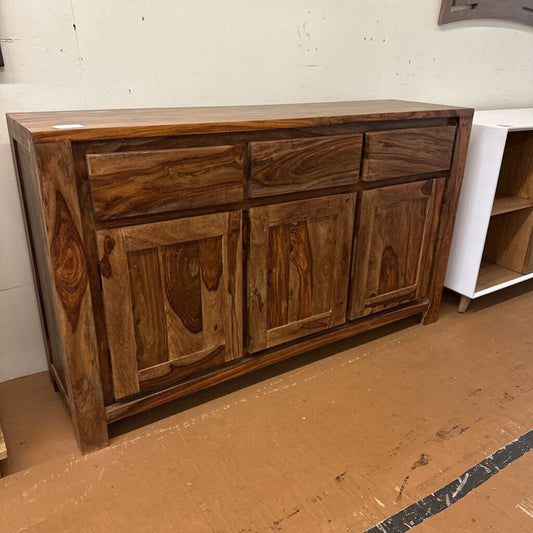 Wooden sideboard with multiple drawers and doors on a cardboard floor.