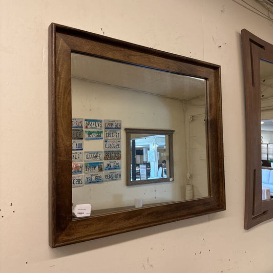 Wooden-framed mirror on a wall with a visible price tag.
