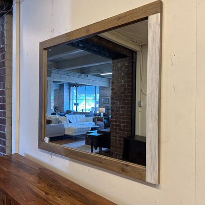 Large rectangular mirror with wooden frame on a wall, reflecting a living room.