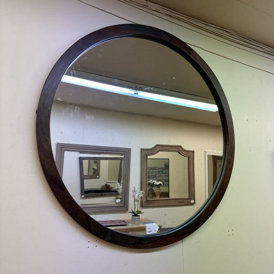 Round wooden-framed mirror on a wall with reflections of other mirrors.