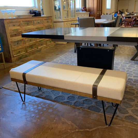 Beige cushioned bench with black straps in a room with a dining table and chairs.