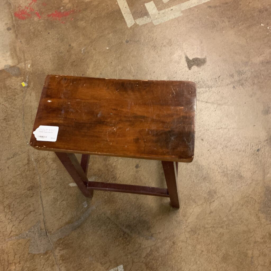 Wooden stool on a concrete floor with a visible tag.