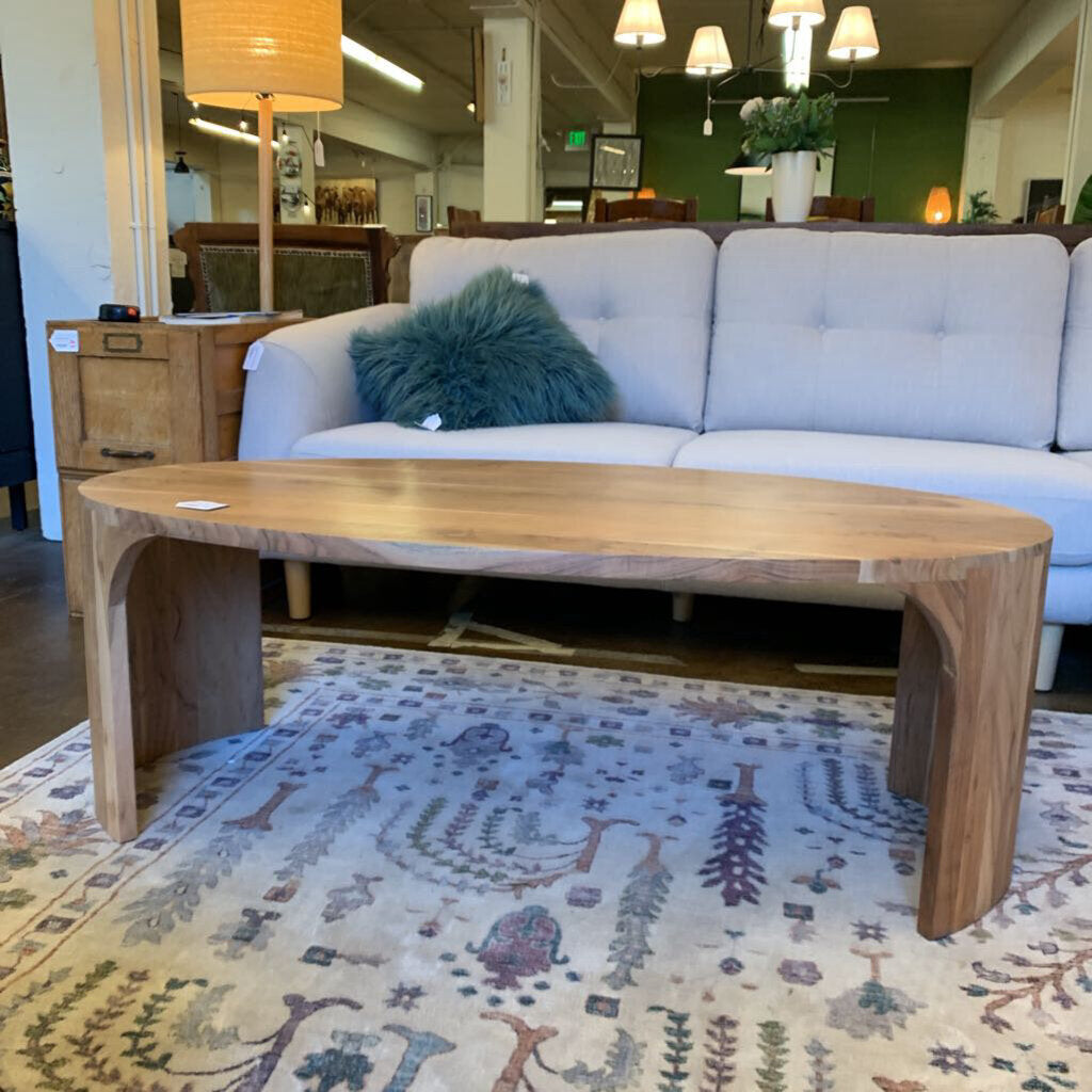 Wooden coffee table in front of a gray sofa with a green pillow on a patterned rug.