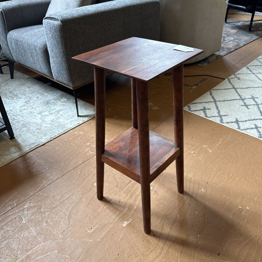 Wooden side table in a living room setting with a gray sofa and patterned rug.