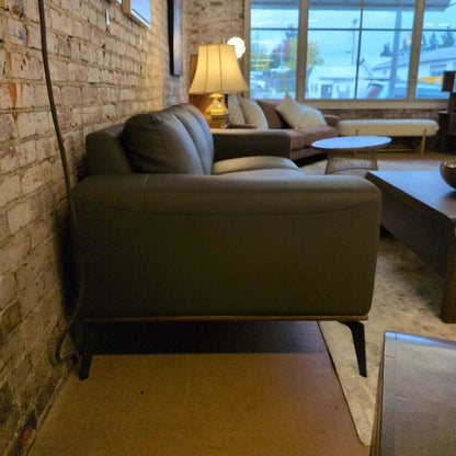 Modern living room with a gray sofa, brick wall, and large windows.