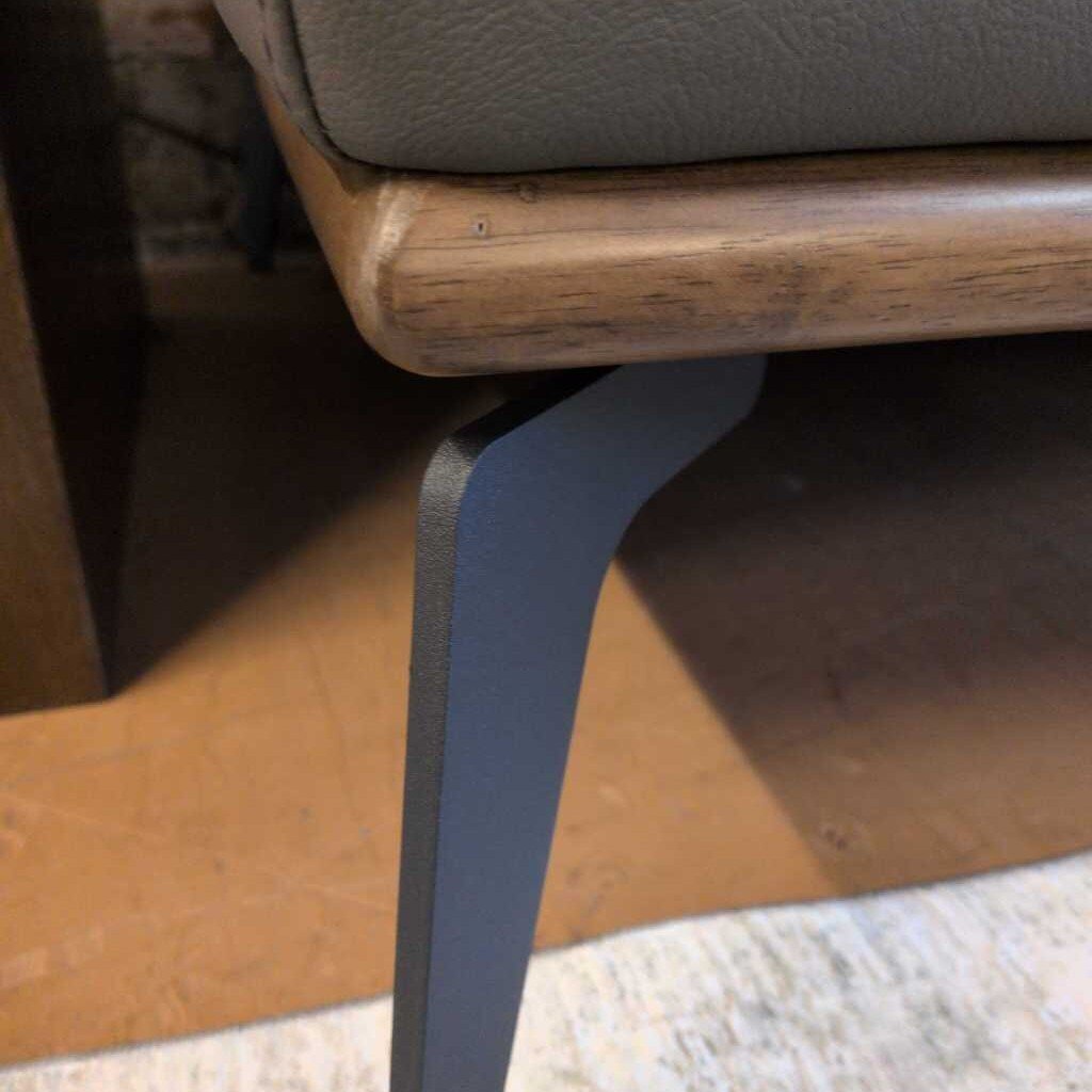 Close-up of a chair leg with a wooden frame and gray cushion.