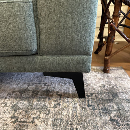 Gray upholstered chair on a patterned rug with wooden legs.