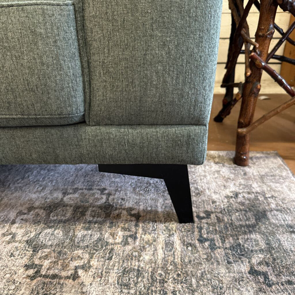 Gray upholstered chair on a patterned rug with wooden legs.