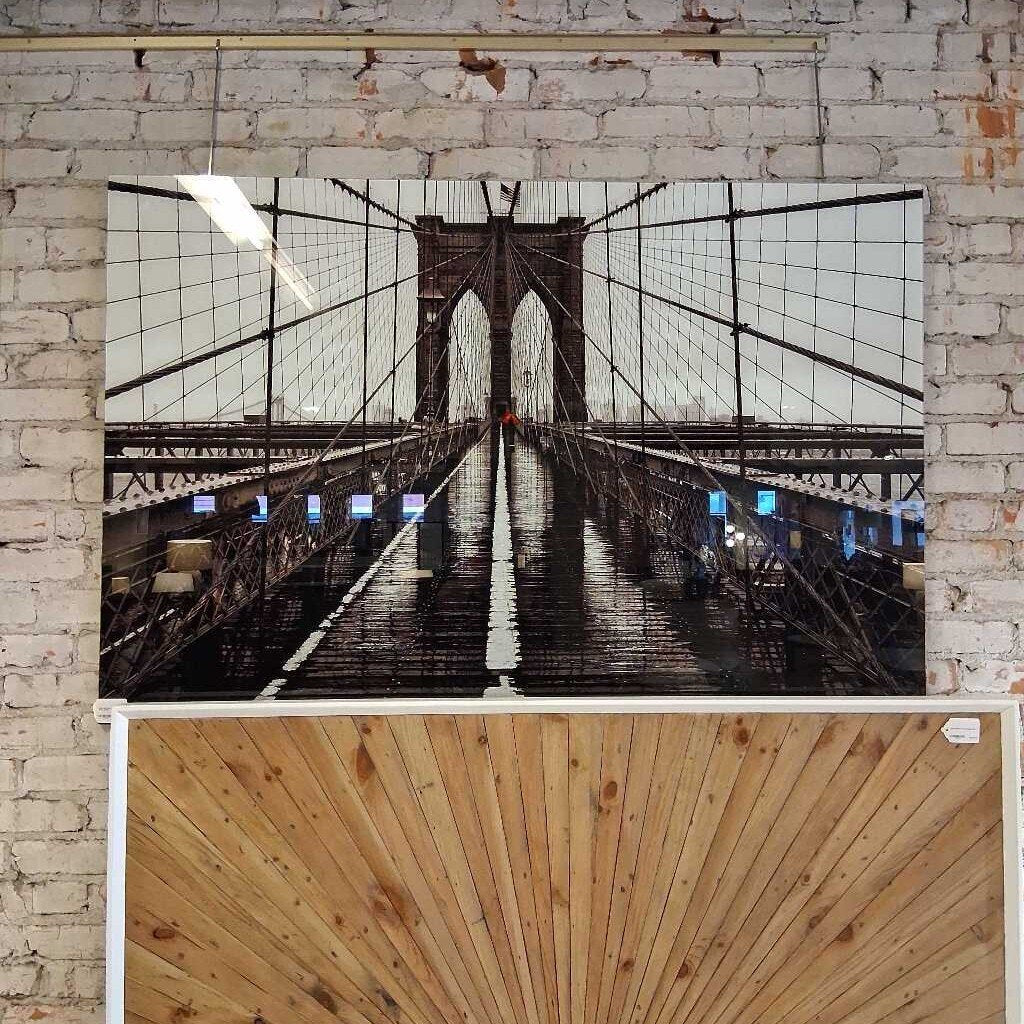 Framed photograph of a bridge with a wooden panel at the bottom on a brick wall.