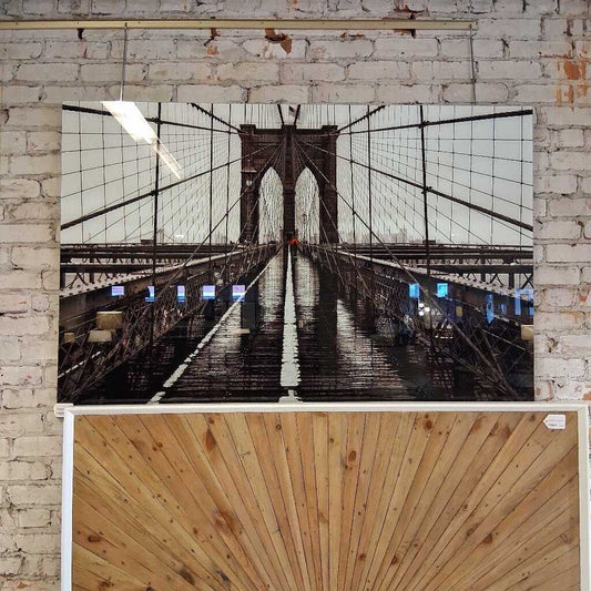 Framed photograph of a bridge with a wooden panel at the bottom on a brick wall.