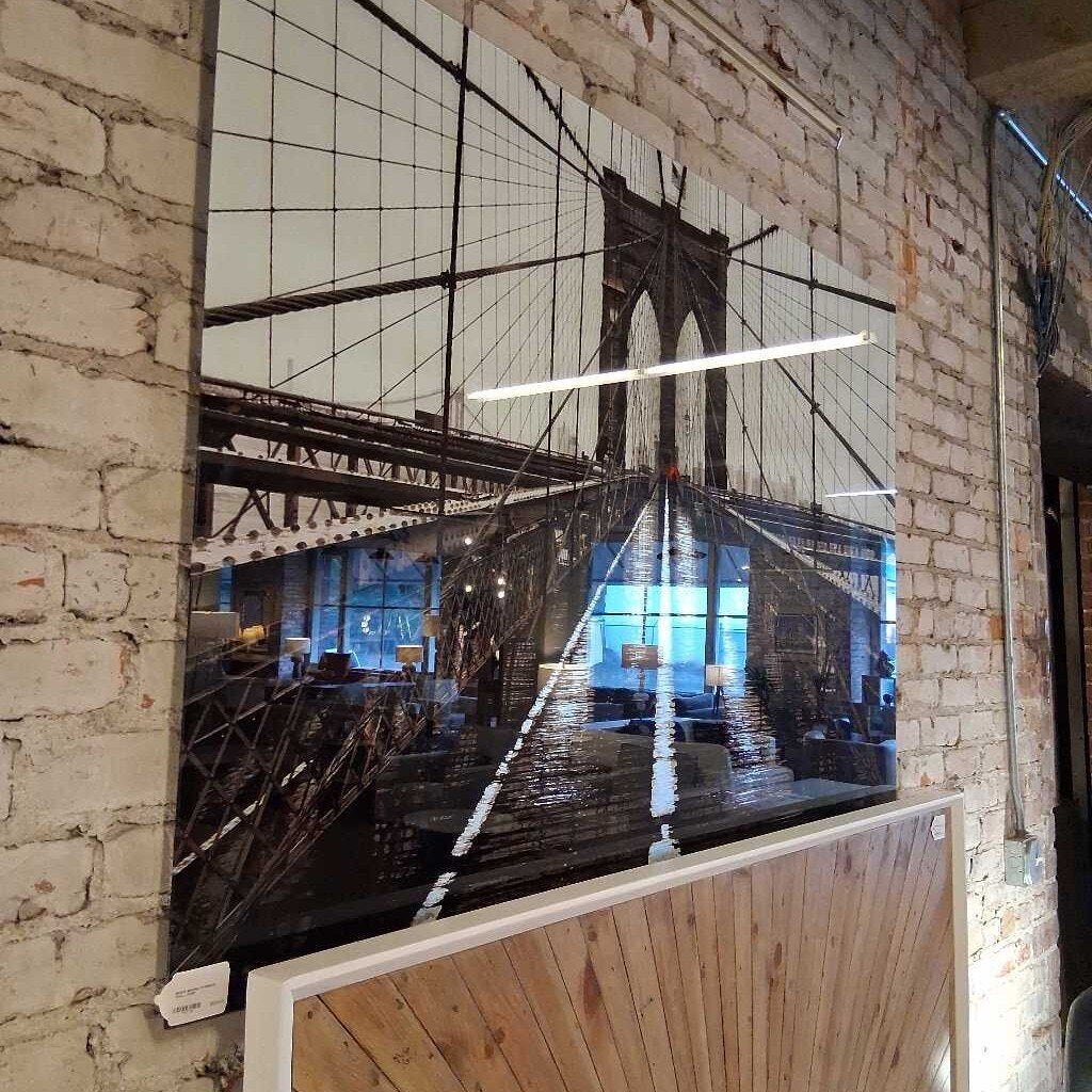 Large mirror reflecting a cityscape with a bridge on a brick wall.