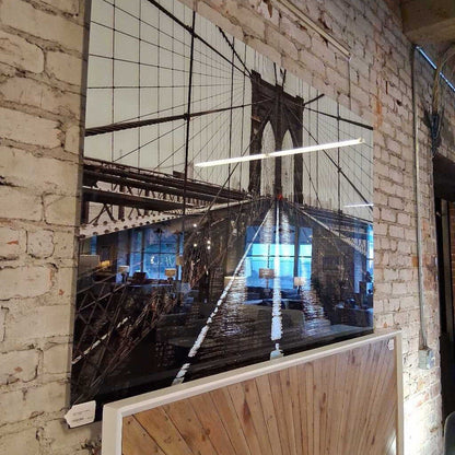 Large mirror reflecting a cityscape with a bridge on a brick wall.