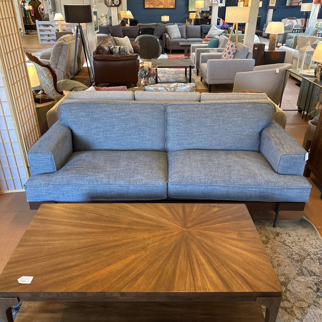 Blue sofa in a showroom with wooden coffee table and various furniture pieces.