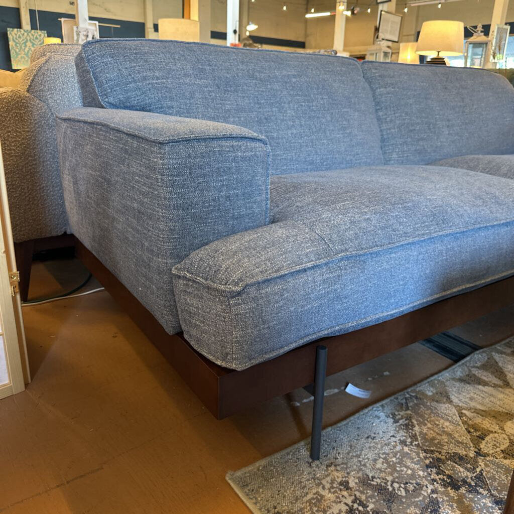 Blue sofa in a store setting with tiled floor and furniture in the background