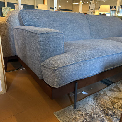 Blue sofa in a store setting with tiled floor and furniture in the background