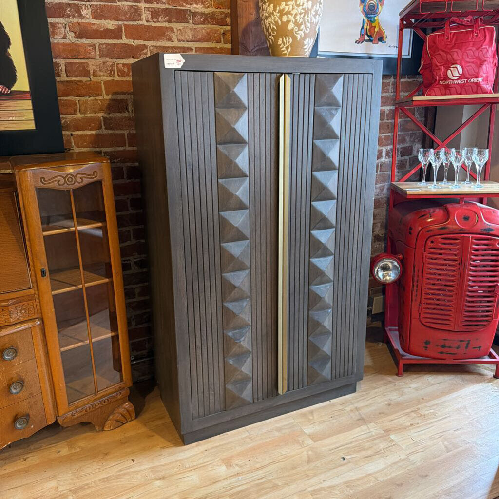 Tall gray cabinet with geometric design in a room with brick wall and wooden floor