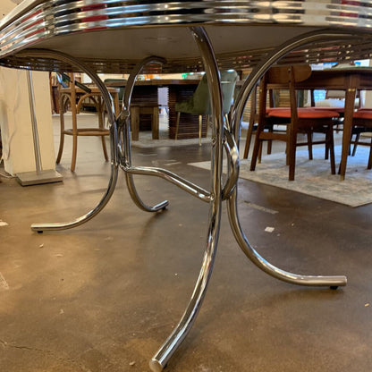 Close-up of a chrome table base in an indoor setting with other furniture.