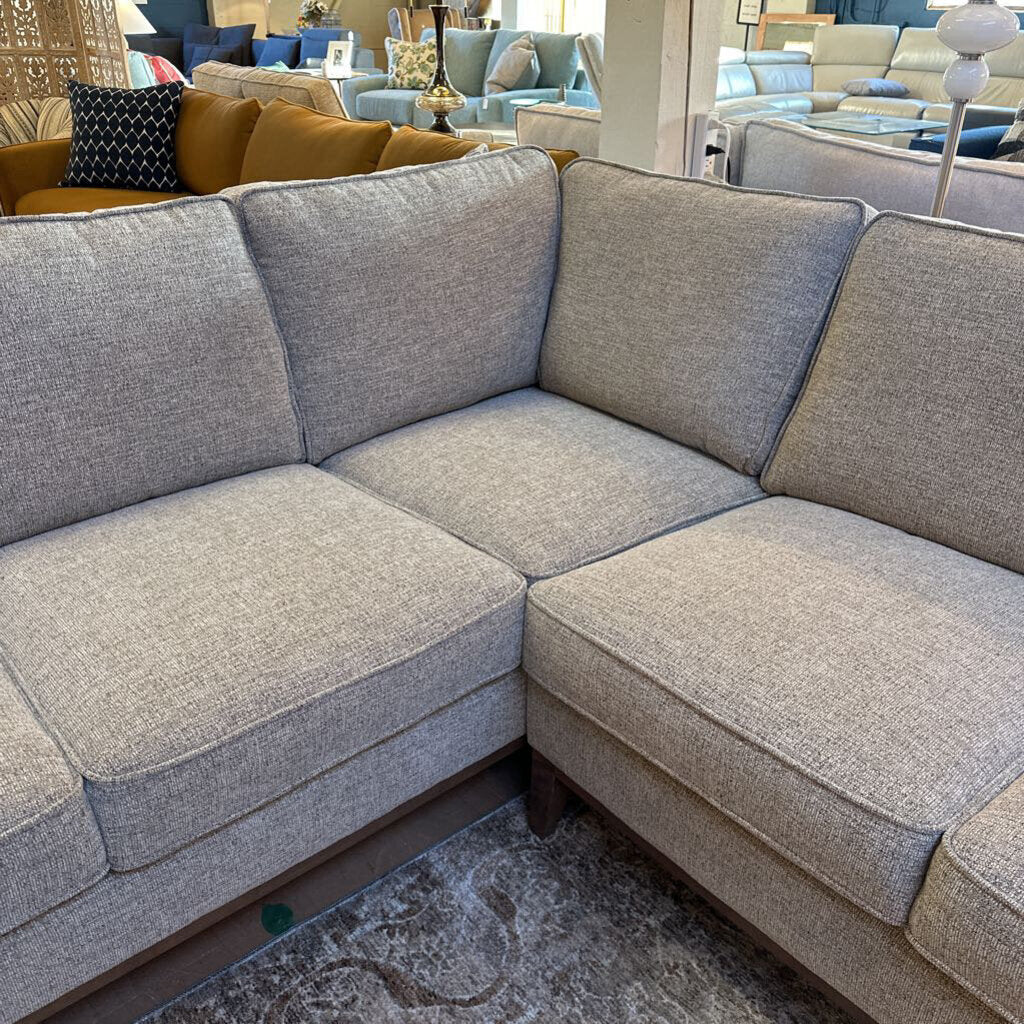 Gray sectional sofa in a showroom setting with other furniture in the background.