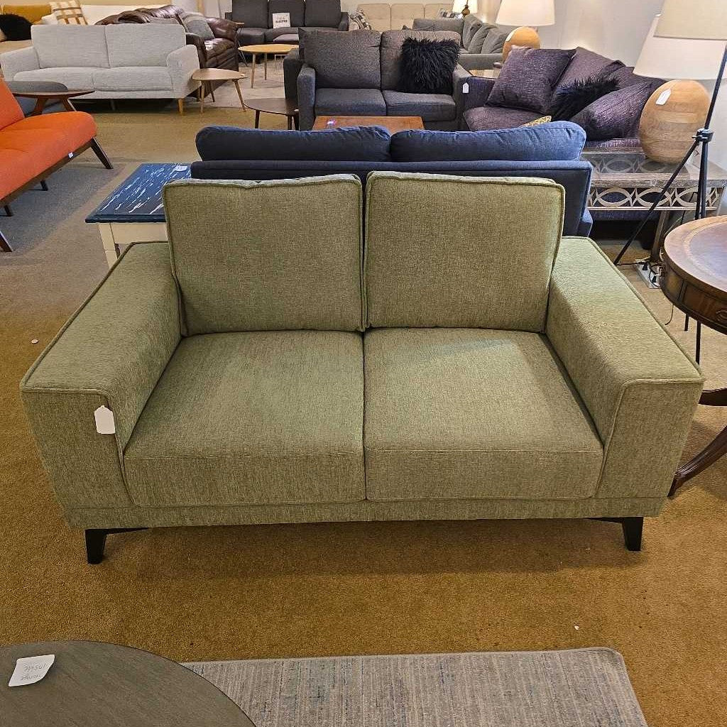 Green sofa in a furniture store with other sofas and tables in the background.