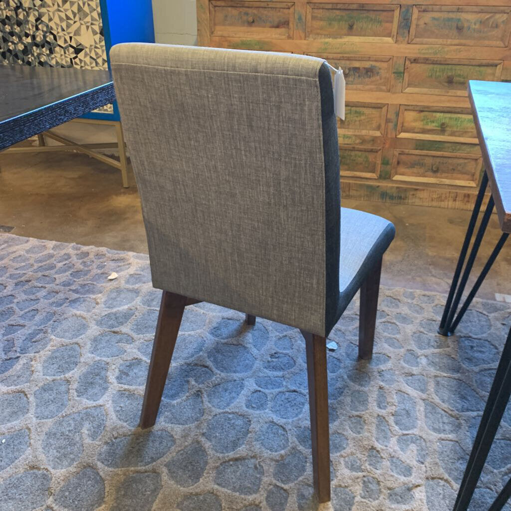 Gray upholstered chair on a stone floor with wooden wall and table in the background