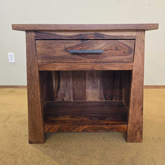 Wooden nightstand with a drawer on a beige carpeted floor.