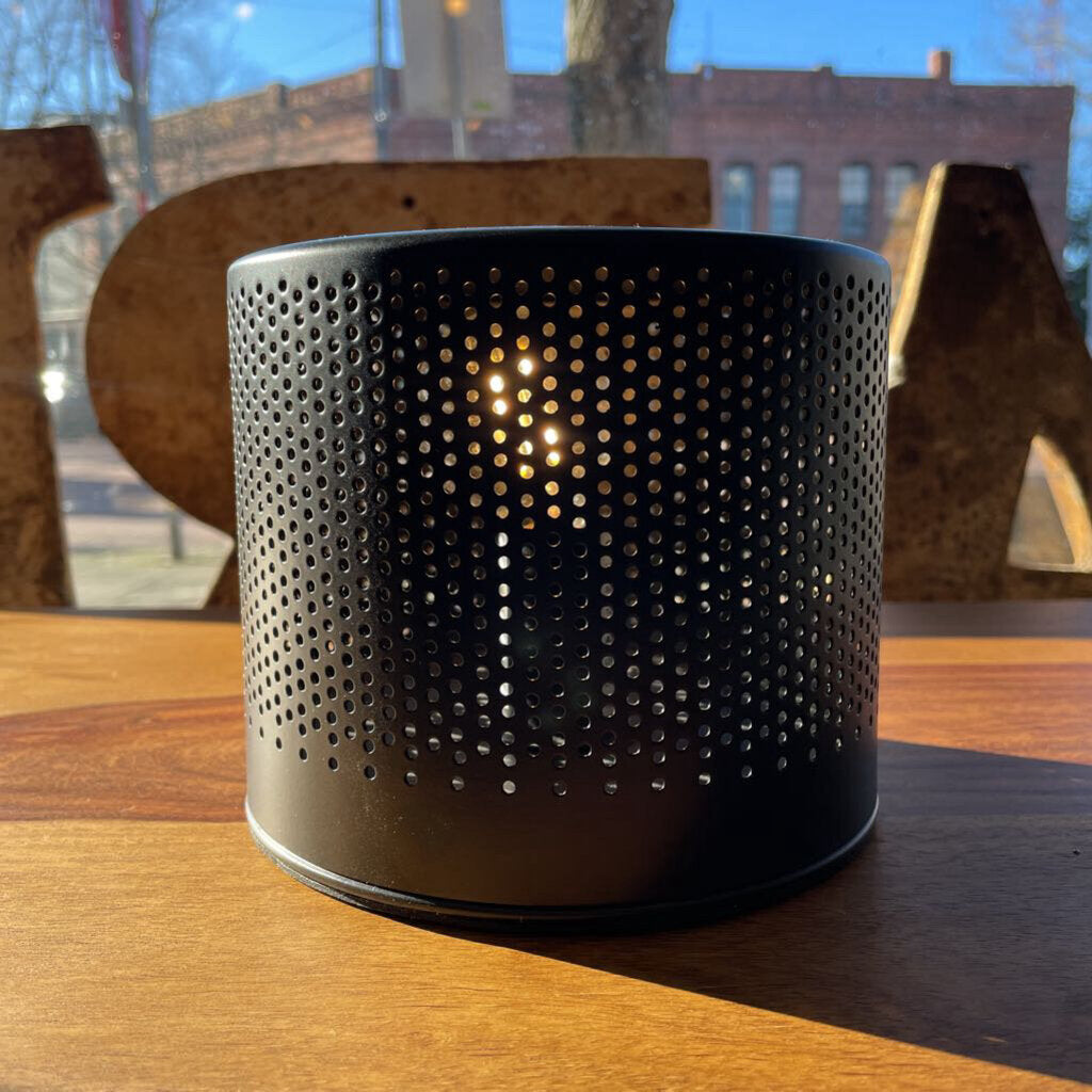Black perforated container with a light inside on a wooden surface