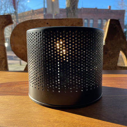 Black perforated container with a light inside on a wooden surface