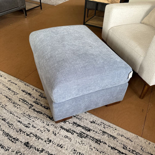 Gray ottoman on a patterned rug with a beige sofa in the background