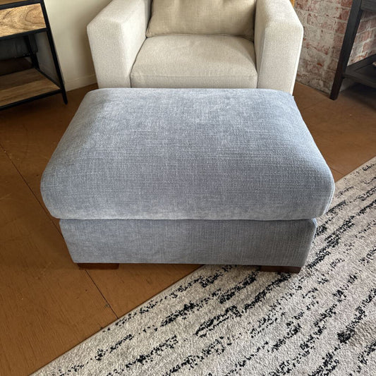 Gray ottoman in a room with a chair and rug.