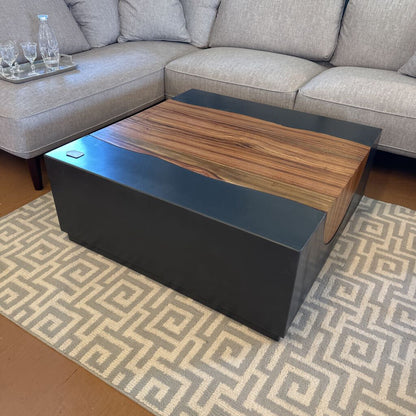 Modern coffee table with wooden top and black base in a living room setting.