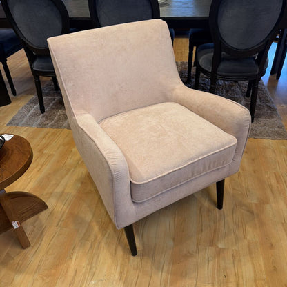 Beige armchair on a wooden floor with other furniture in the background