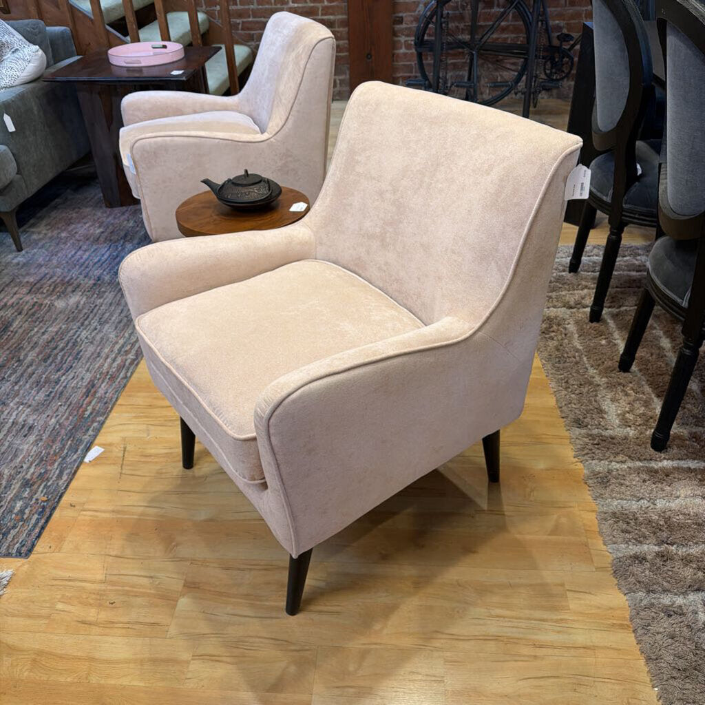 Beige armchair in a showroom setting with wooden floor and other furniture.