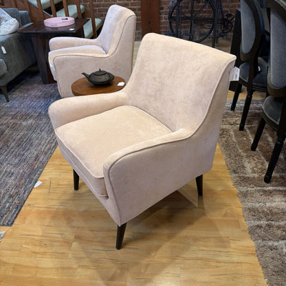 Beige armchair in a showroom setting with wooden floor and other furniture.