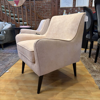 Beige armchair on a wooden floor with a blurred background of furniture and decor.