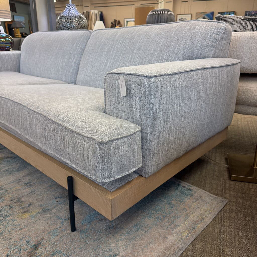 Gray fabric sofa with wooden legs in a showroom setting