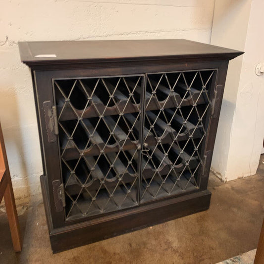 Dark wooden wine rack with lattice design doors against a white wall.