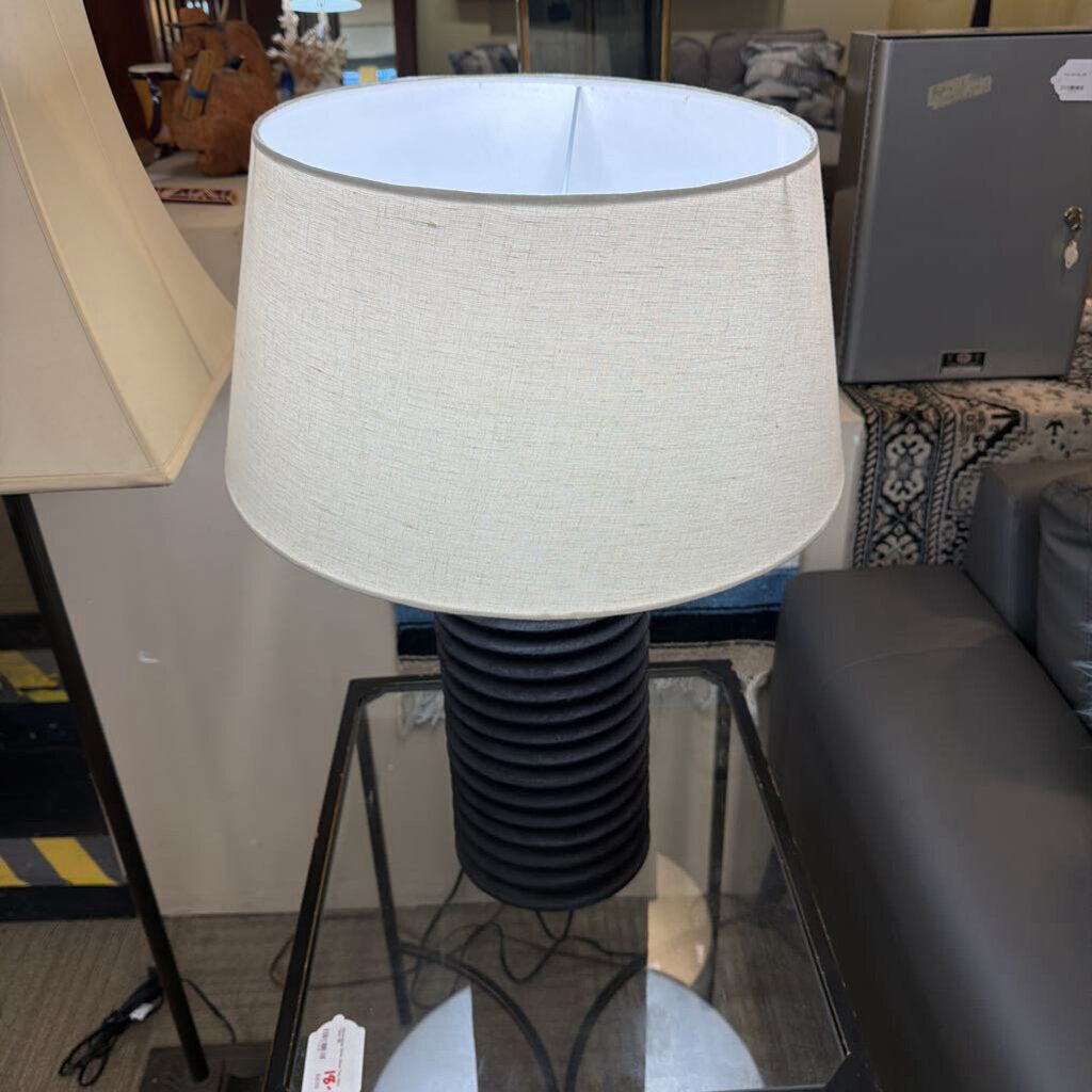 Table lamp with a white shade and black base on a glass table in an indoor setting.