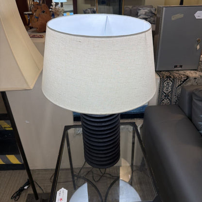 Table lamp with a white shade and black base on a glass table in an indoor setting.
