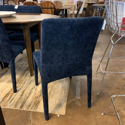 Blue velvet chair in a showroom setting with wooden tables and chairs.
