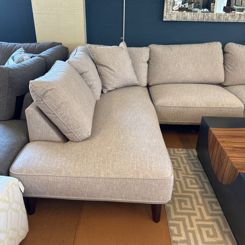 Beige sectional sofa in a living room setting with a blue wall and wooden coffee table.