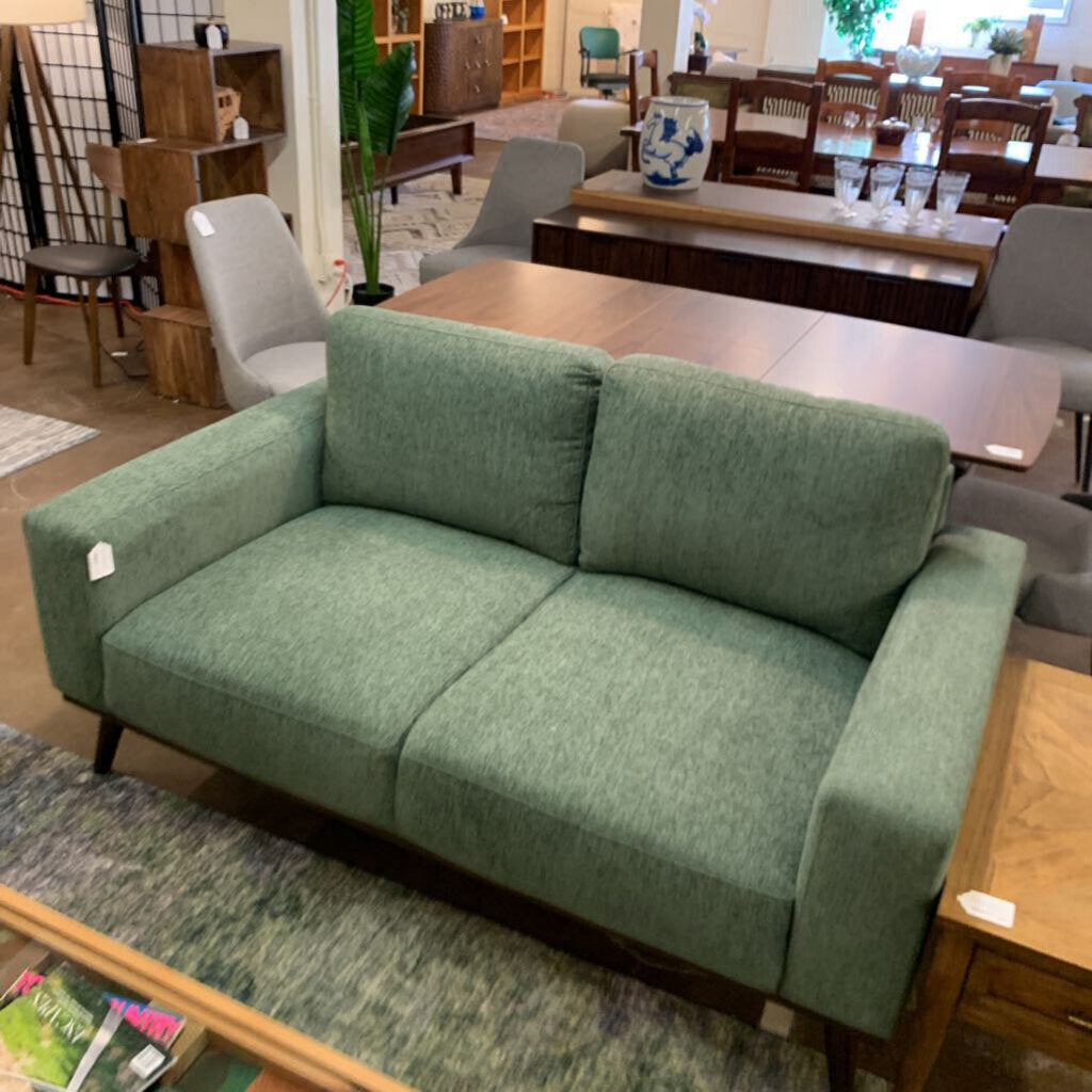 Green sofa in a furniture store setting with tables and chairs around