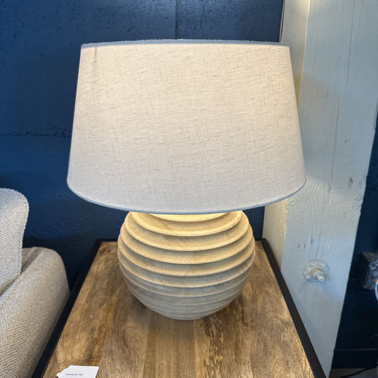 Table lamp with a textured white shade on a wooden table against a blue wall.