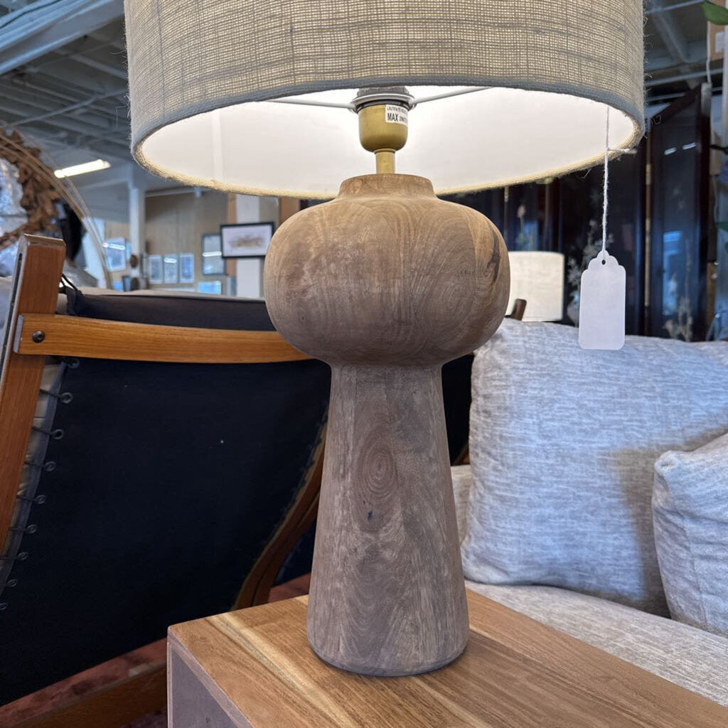 Wooden table lamp with a gray shade on a wooden surface in a store setting.