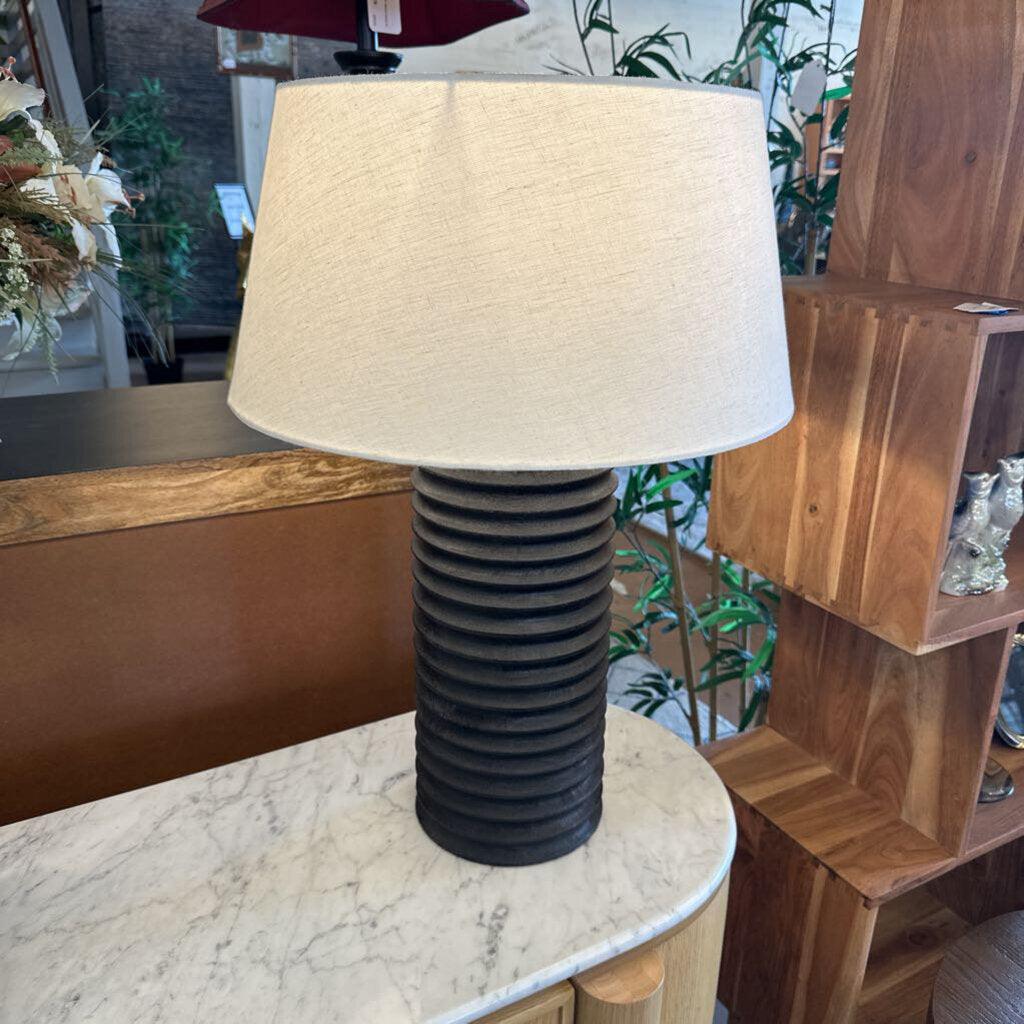 Table lamp with a ribbed black base and beige lampshade on a marble surface.