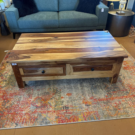Wooden coffee table with drawers on a patterned rug, with a blue sofa in the background.
