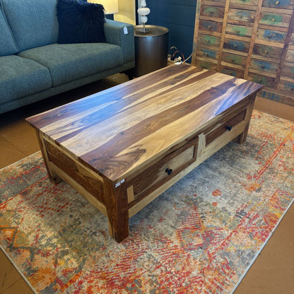 Wooden coffee table in a living room setting with a sofa and decorative items.