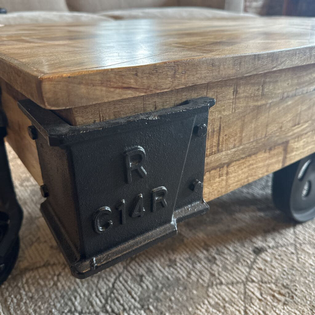 Wooden cart with a metal bracket featuring the letters 'R' and 'Q14R' on a textured surface.