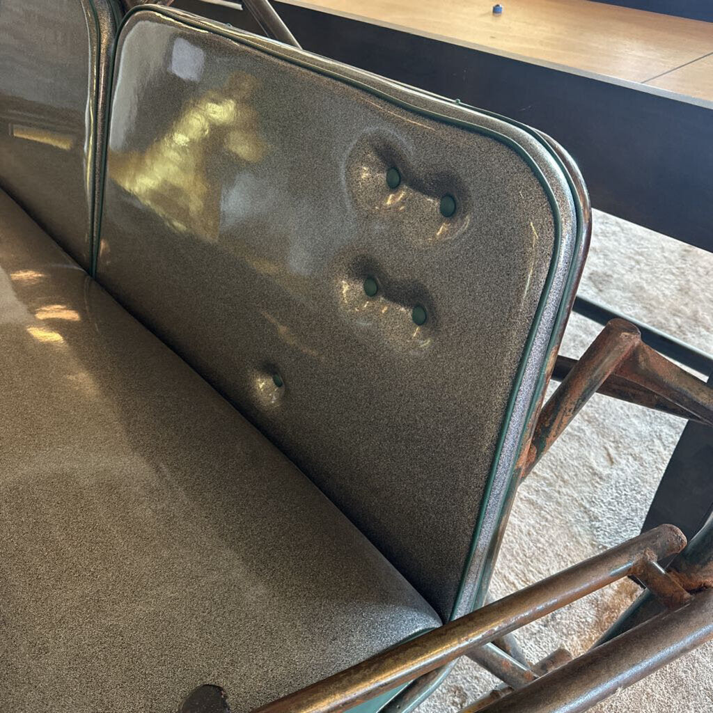 Rust-colored metal chair with a worn cushion on a concrete floor.