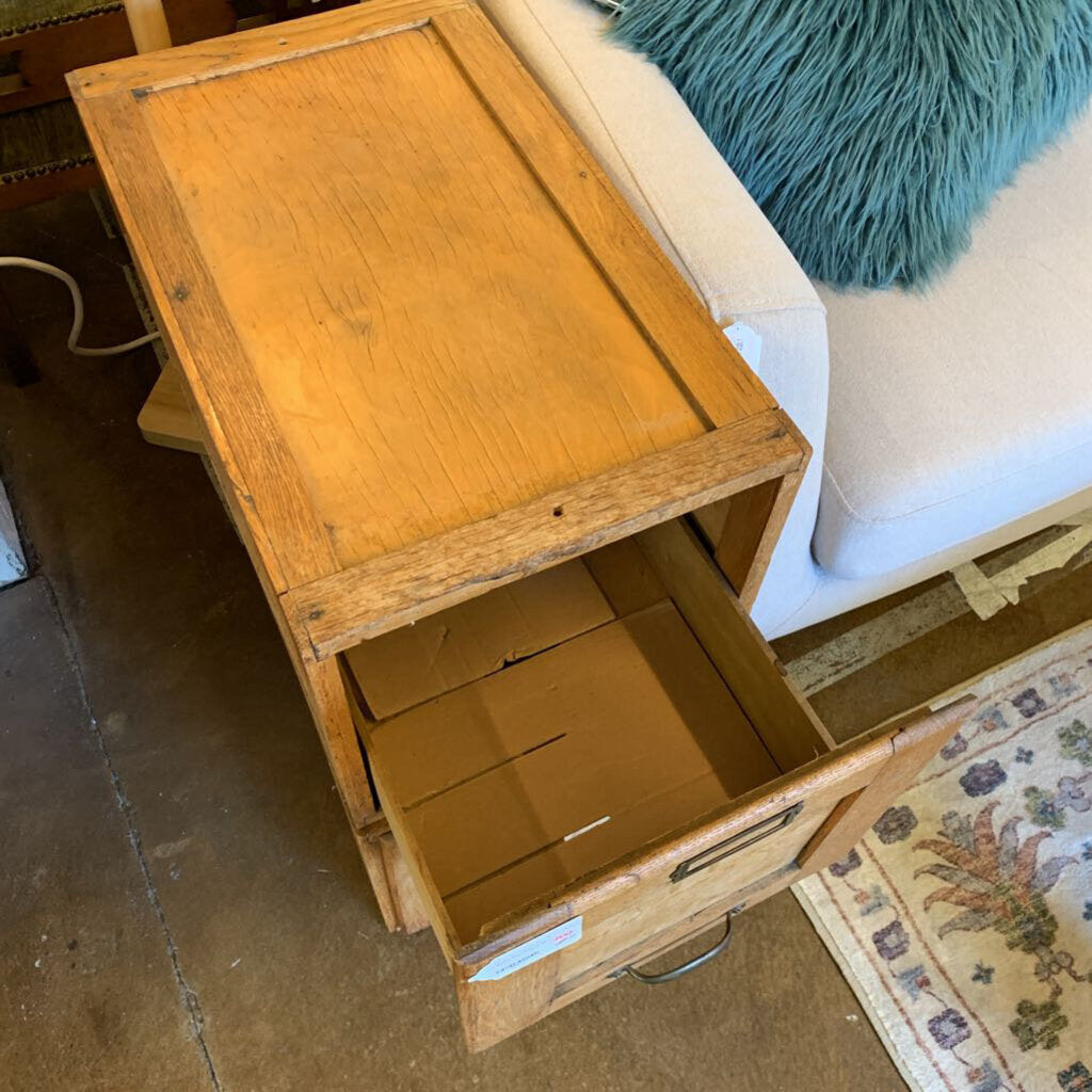 Wooden cabinet with open drawer on a wooden floor next to a white couch with a blue pillow.